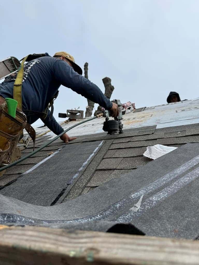 Crew member in a cap on a steep roof of architectural shingles